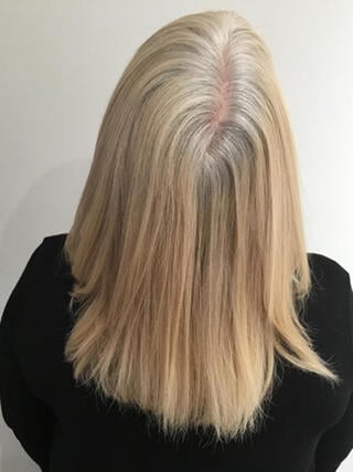 Vorher-Foto: Rückansicht einer Frau mit mittellangen blonden Haaren mit schwarzen Strähnen vor dem Färben.