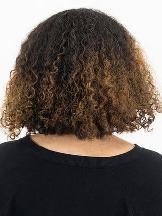 Vorher Foto: Rückansicht einer Frau mit kurzen, lockigen schwarzen Haaren mit einem herausgewachsenen Ansatz vor dem Färben.
